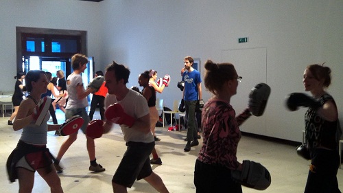 A group of people sparring with boxing gloves and pads in an art gallery