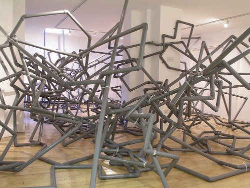 A room filled with a twisting sculpture made of grey plumbers' pipes